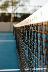 A close-up view of a tennis net with a blurred blue court and background.