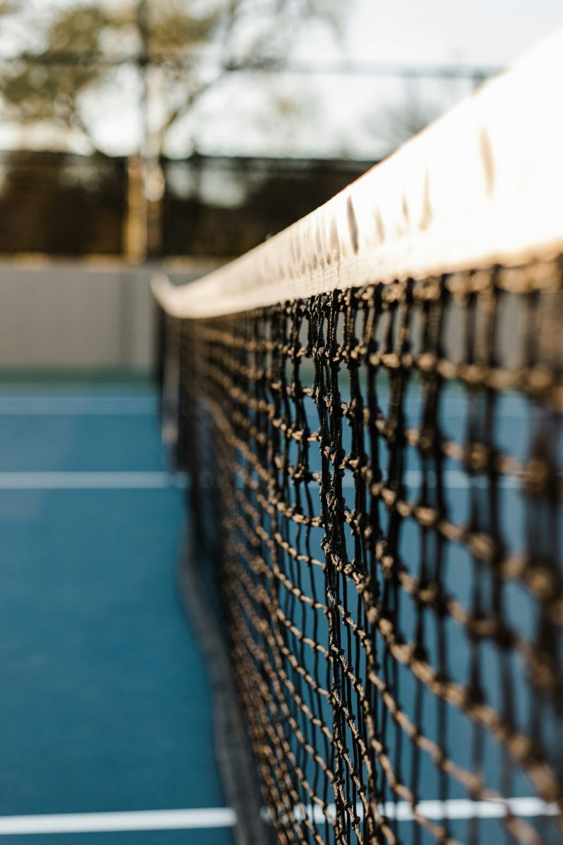 A close-up view of a tennis net with a blurred blue court and background.