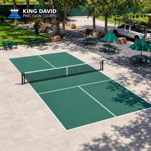 Two adjacent green pickleball courts with a central net are installed on a concrete patio surrounded by picnic tables and umbrellas.